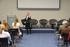 Na środku auli stoi Pani i przemawia przed uczestnikami